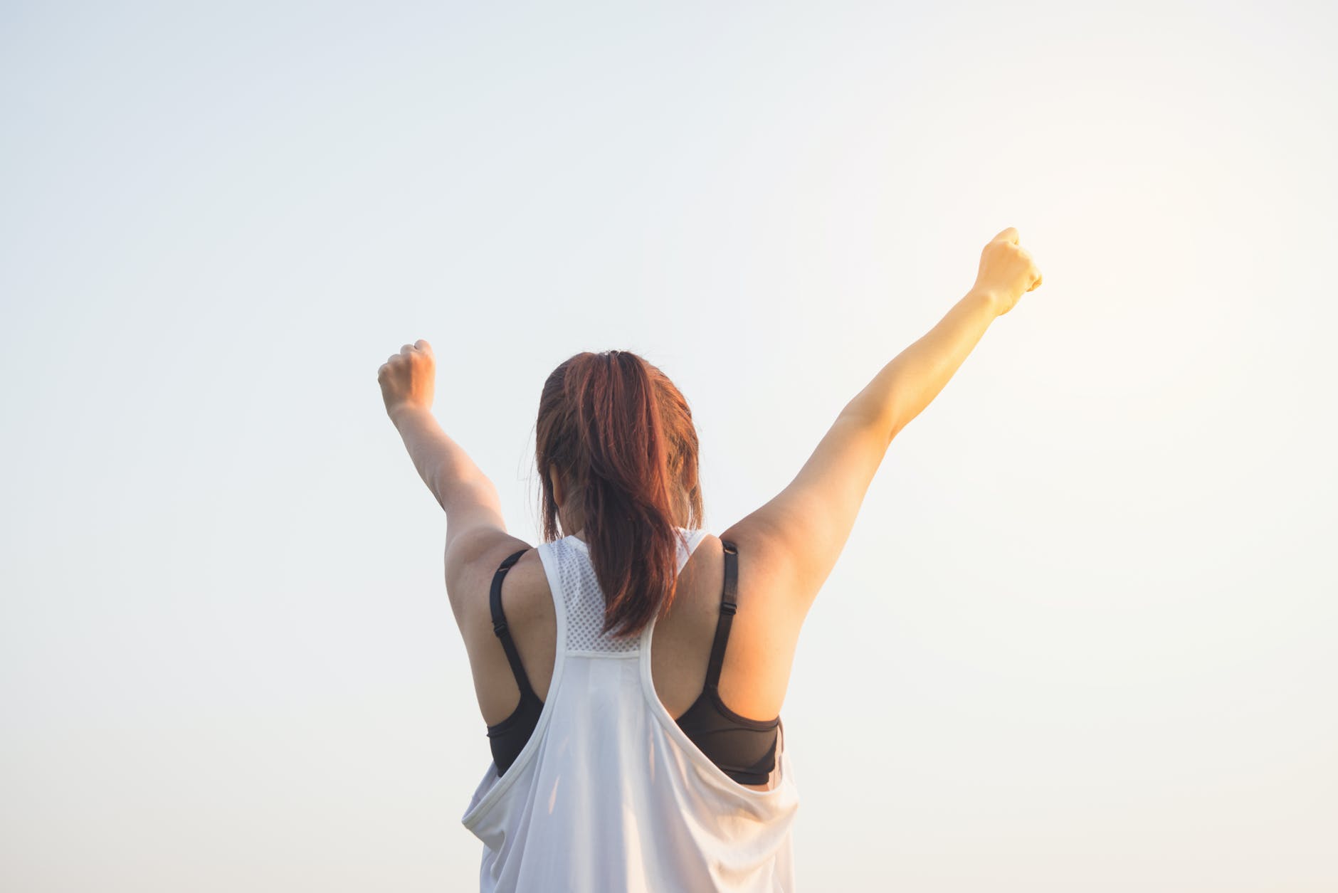 woman wearing black bra and white tank top raising both hands on top