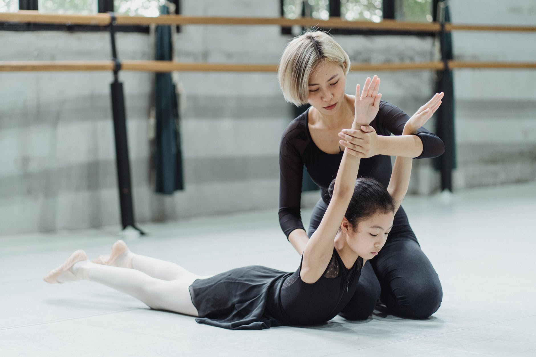 ethnic ballet teacher supporting girl while performing ballet exercise