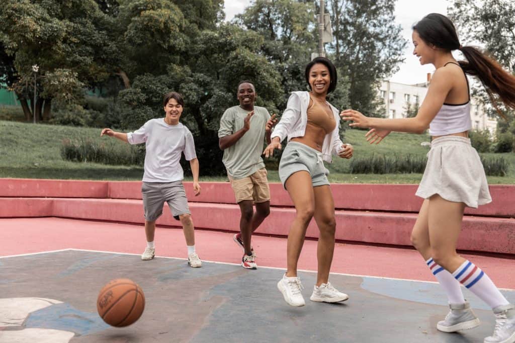 delighted multiethnic friends playing basketball in park