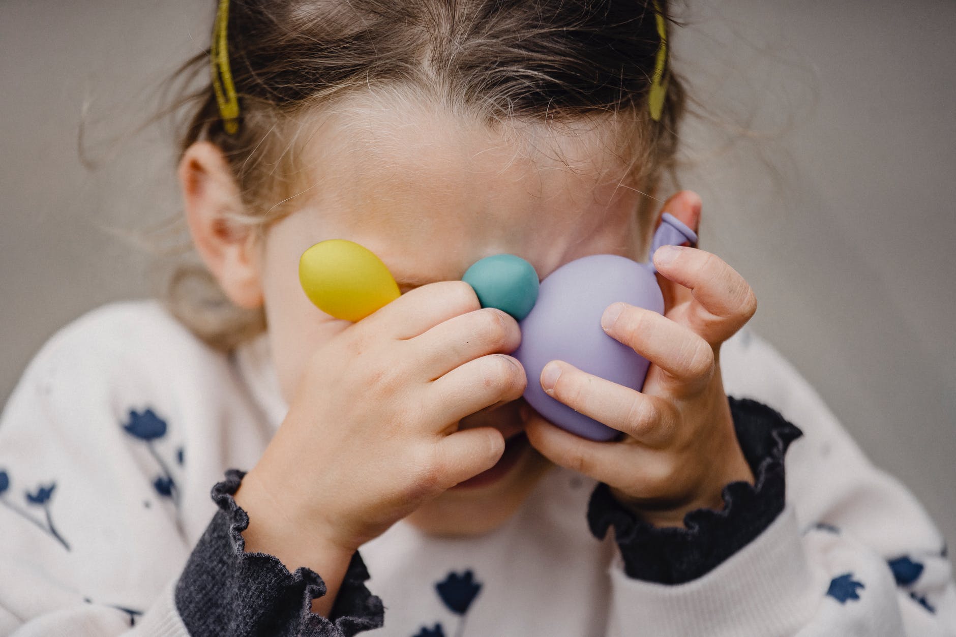 unrecognizable girl covering face with assorted balloons on street