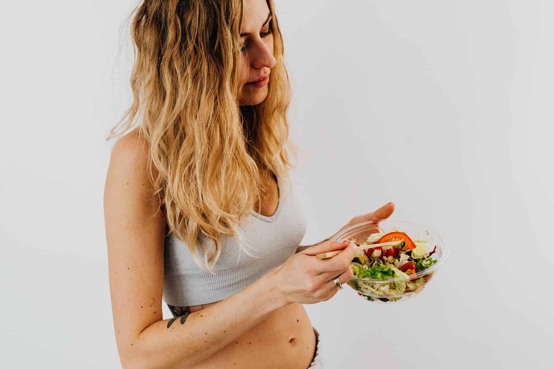 woman in white sports bra holding a bowl of salad