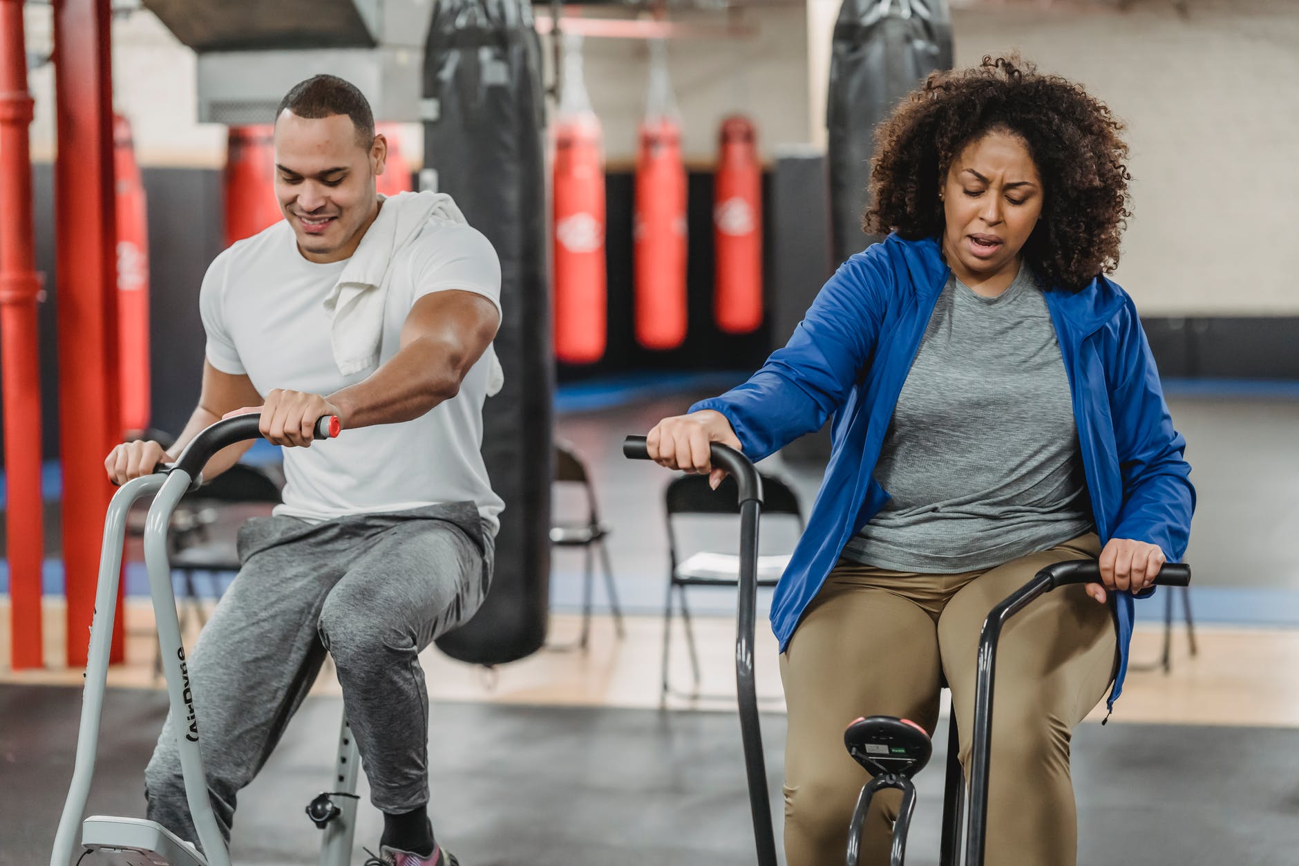 plump black woman and muscular sportsman cycling in gym