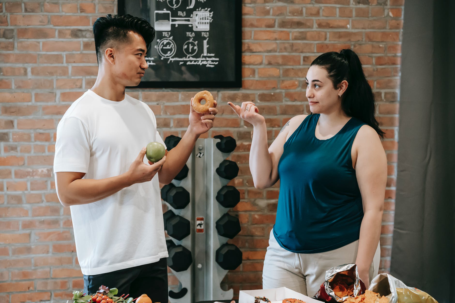 asian instructor with food and ethnic plump woman looking at each other in gym