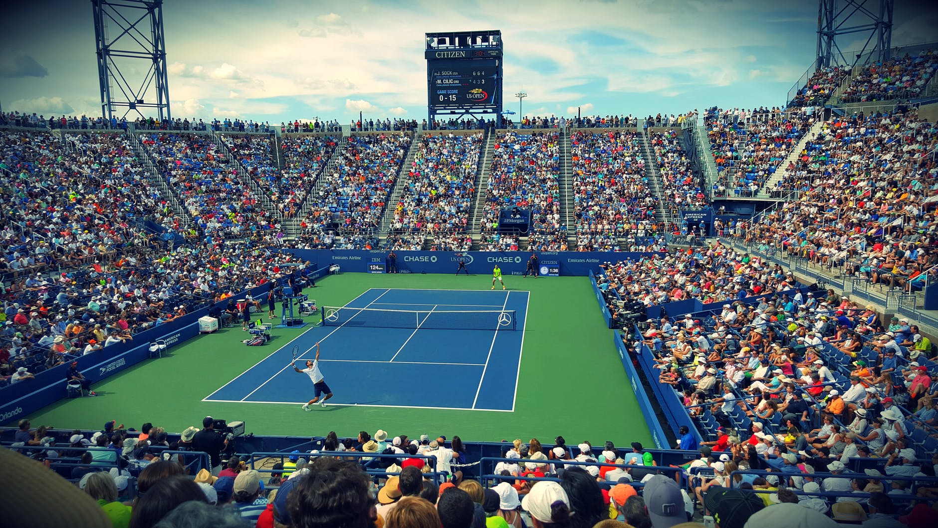 people sitting on bench watching tennis event on field during daytime