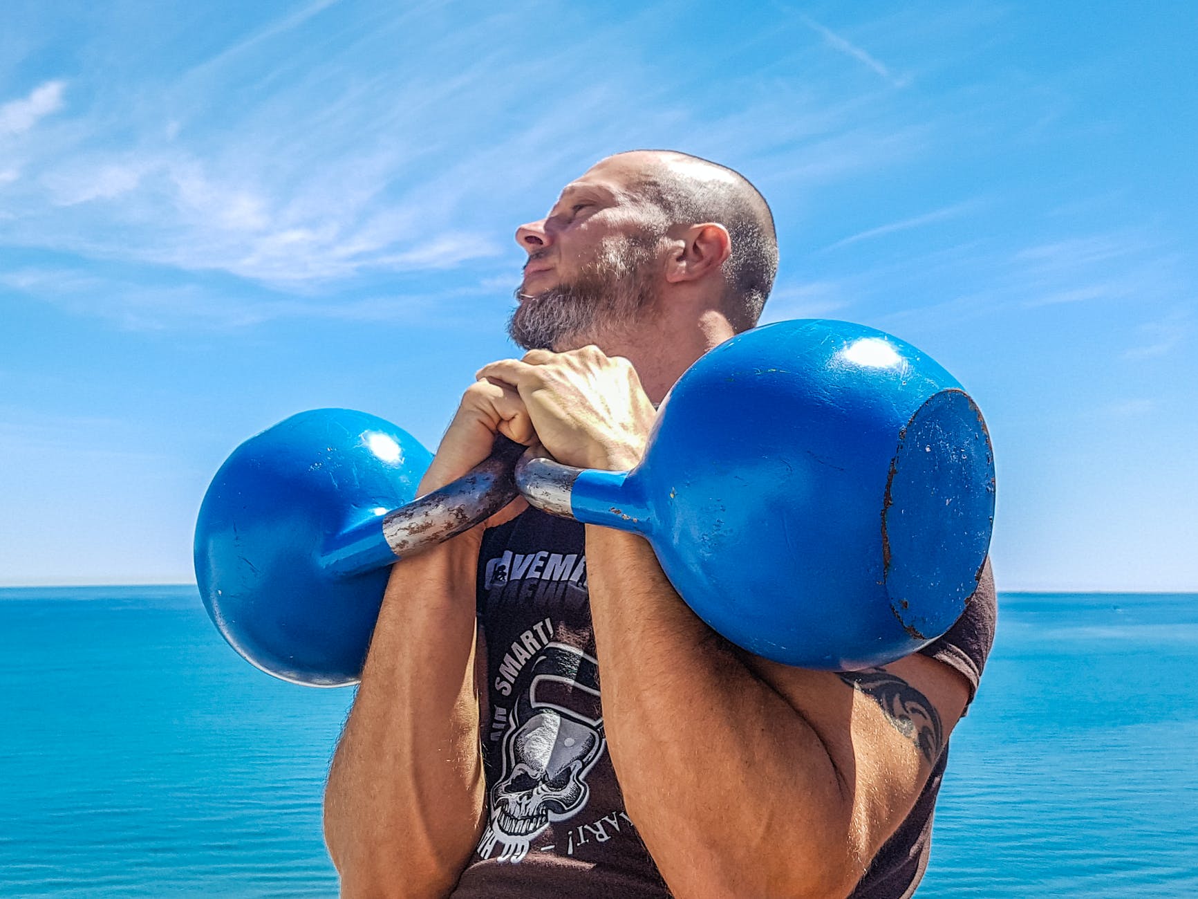 man lifting pair of blue kettlebells